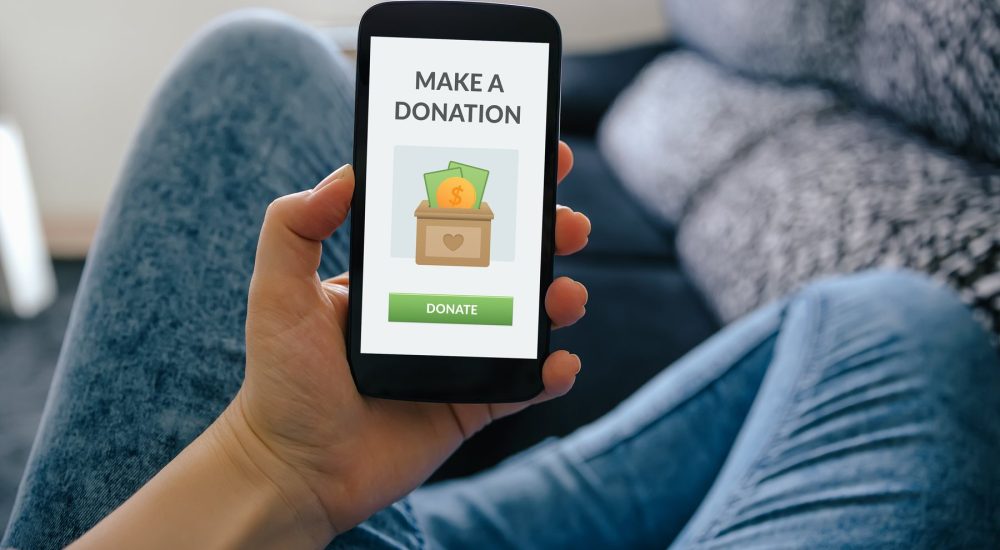 Closeup Of A Person’s Hand Holding A Phone, Promoting Charitable Donations For Tax Deductions.