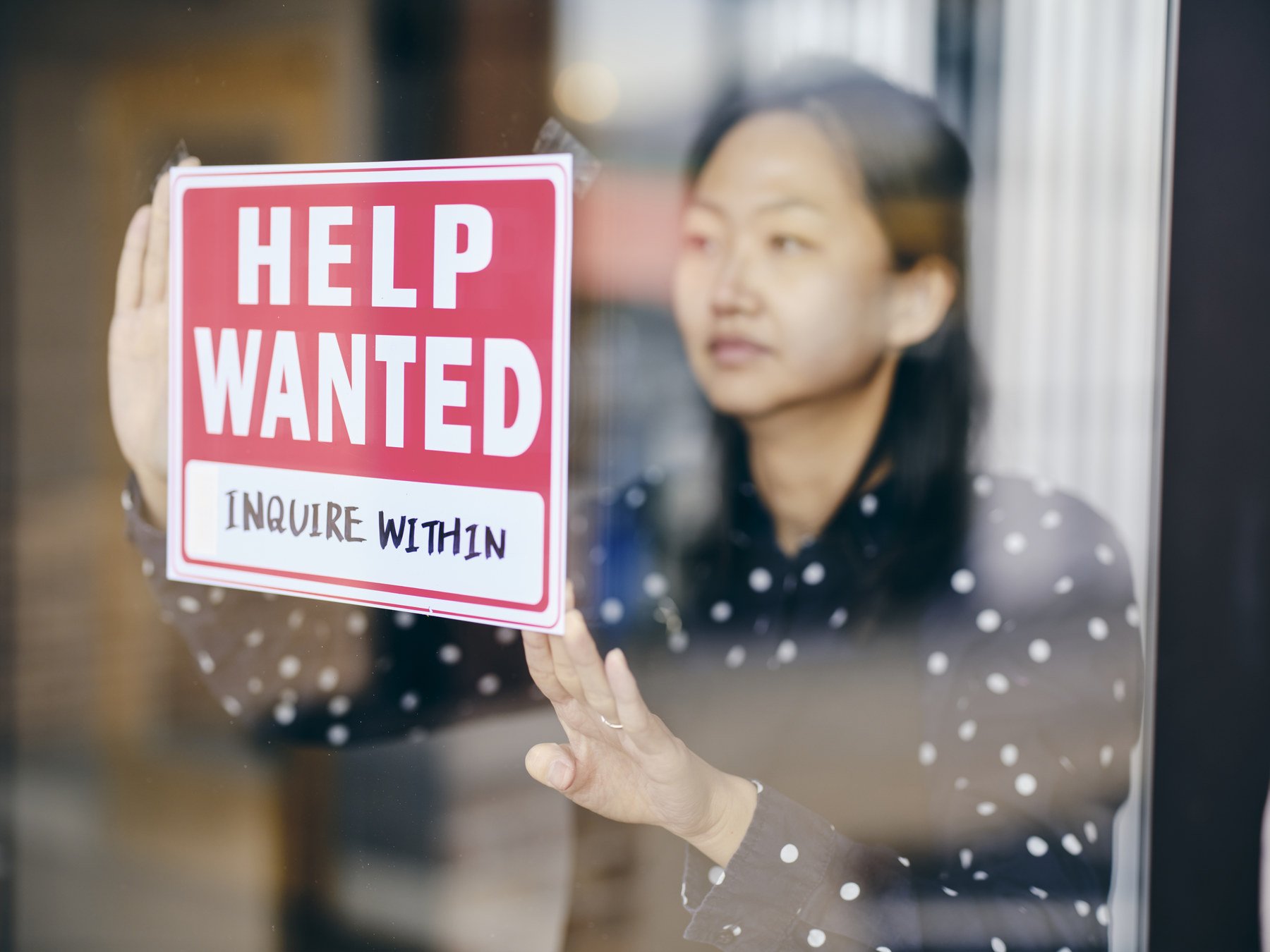A small business owner putting up a help wanted sign in her store window