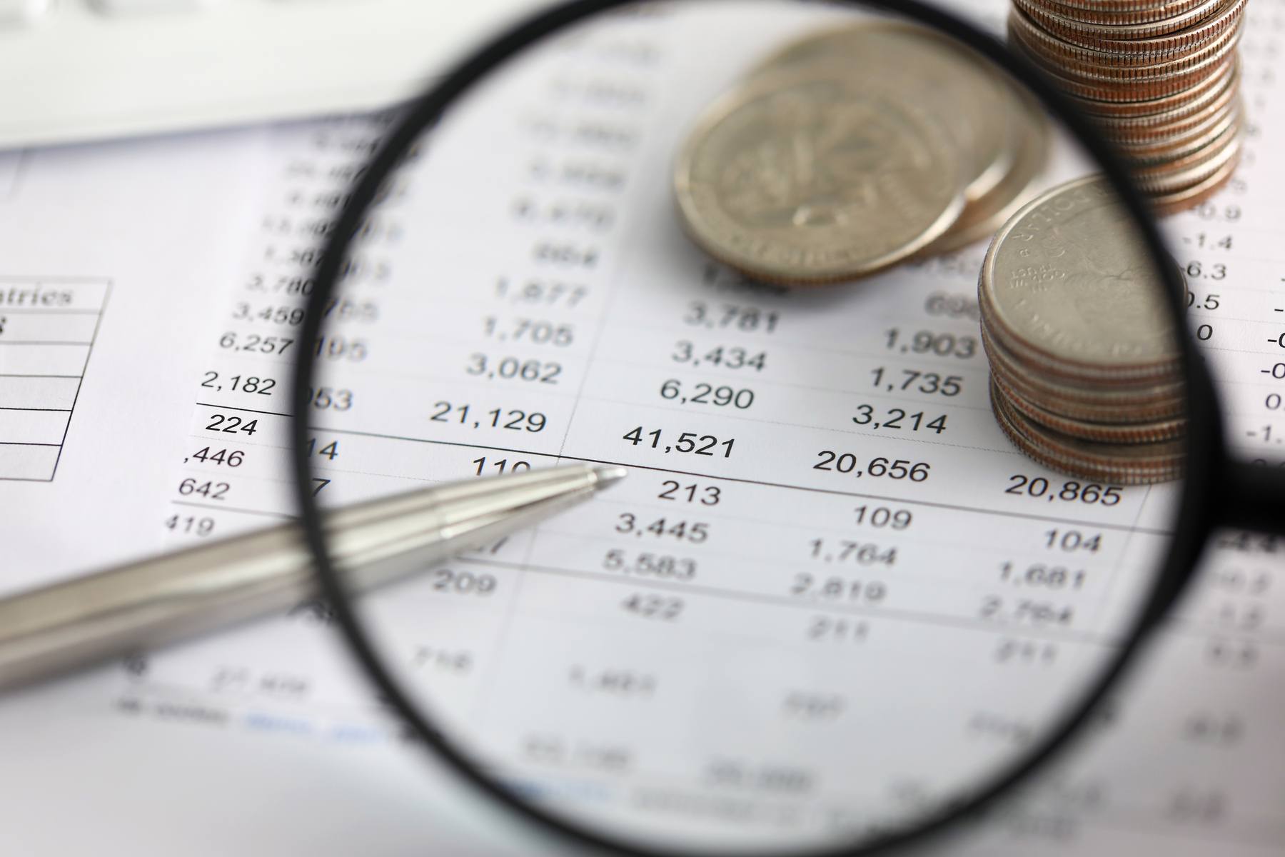 View of financial fraud ledger details in a table through a magnifying glass with coins in the background