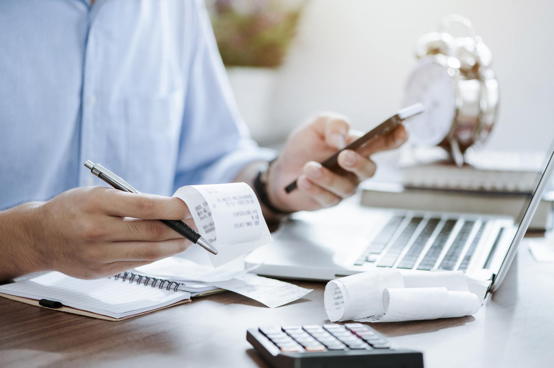 Man holding pen with bills, receipts, laptop, and calculator on his desk